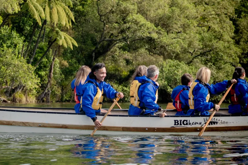 Guests paddling the Big Kanu past native bush on Lake Rotoiti