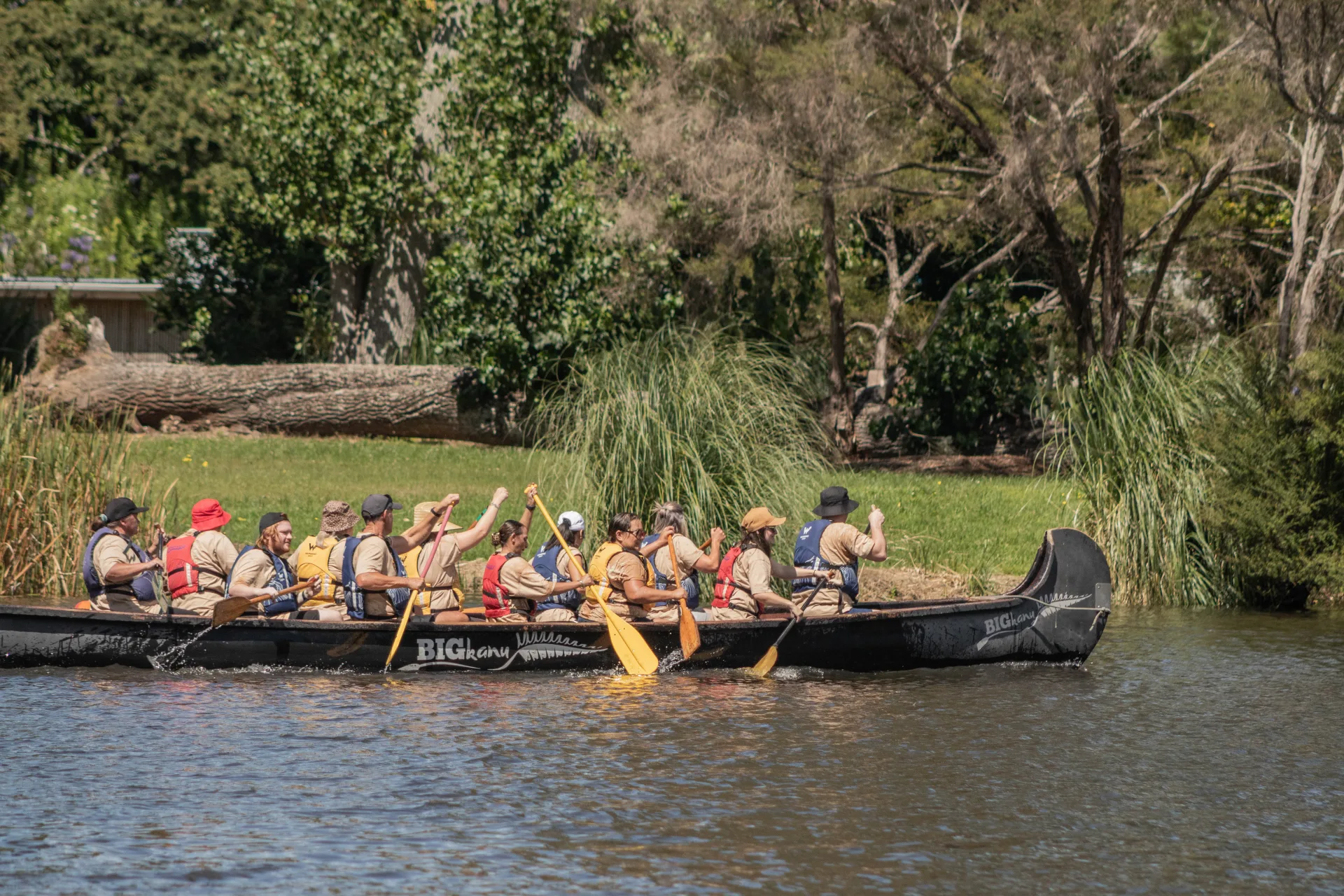 A team paddles a long waka canoe across the river